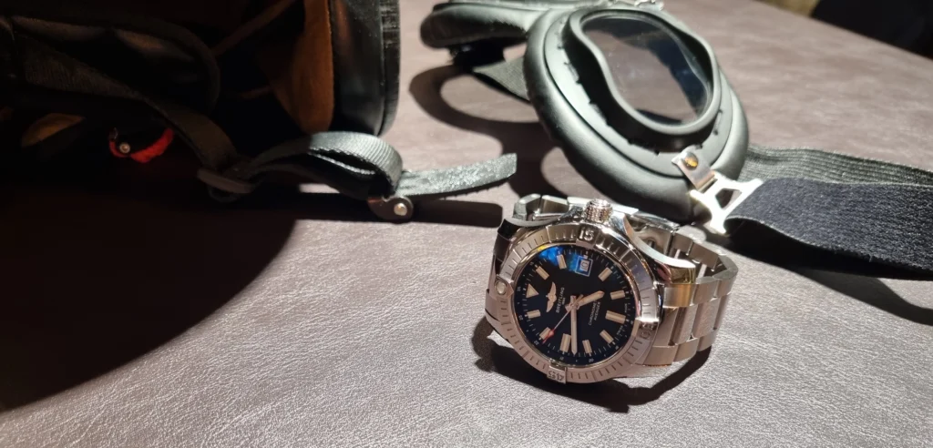 Breitling Avenger 43 fekete számlapos óra egy pilótasisak és egy pilótaszemüveg társaságában.