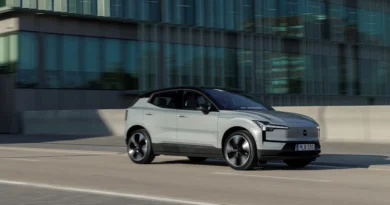 Szürke Volvo EX30 városban, egy üvegépület előtt halad az úton