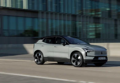 Szürke Volvo EX30 városban, egy üvegépület előtt halad az úton
